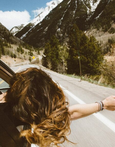woman riding on vehicle putting her head and right arm outside the window while travelling the road
