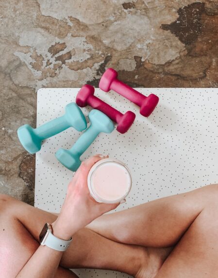 person holding white liquid filled cup above two pairs of dumbbells